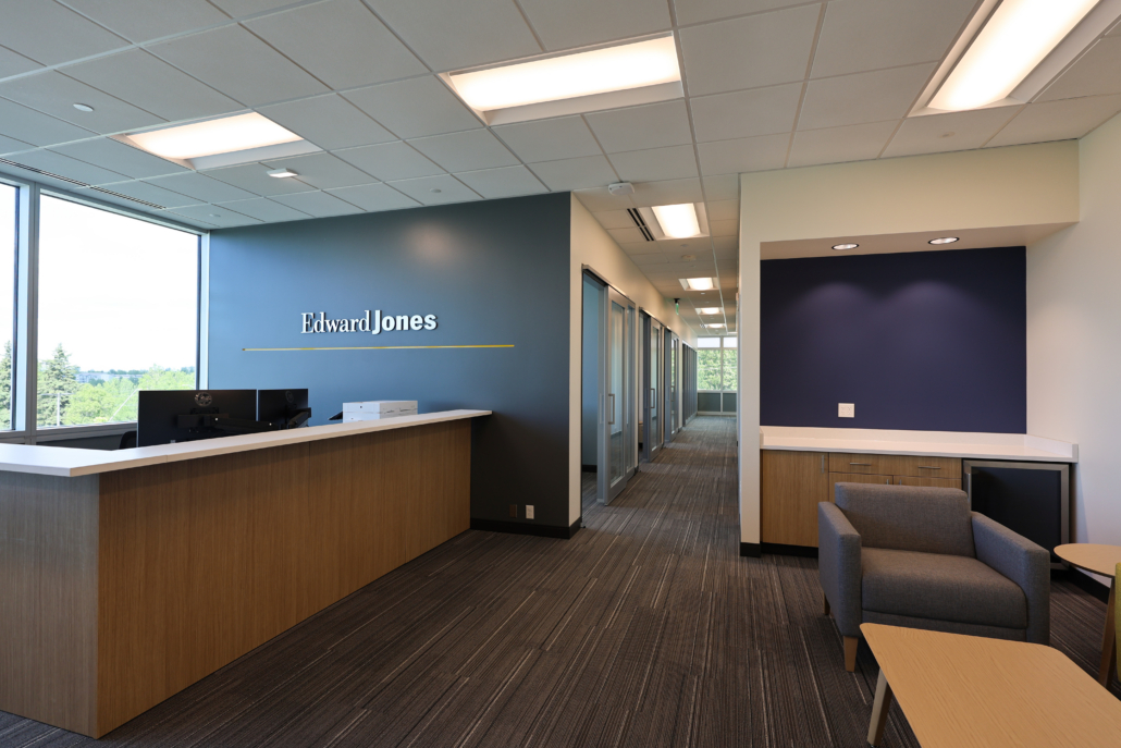 Edward Jones Anchorage Office in SIRI building showing reception desk, Edward Jones logo on the wall, reception lounge or waiting area with coffee table and lounge seating, and hallway with modular wall glass store fronts for conference rooms